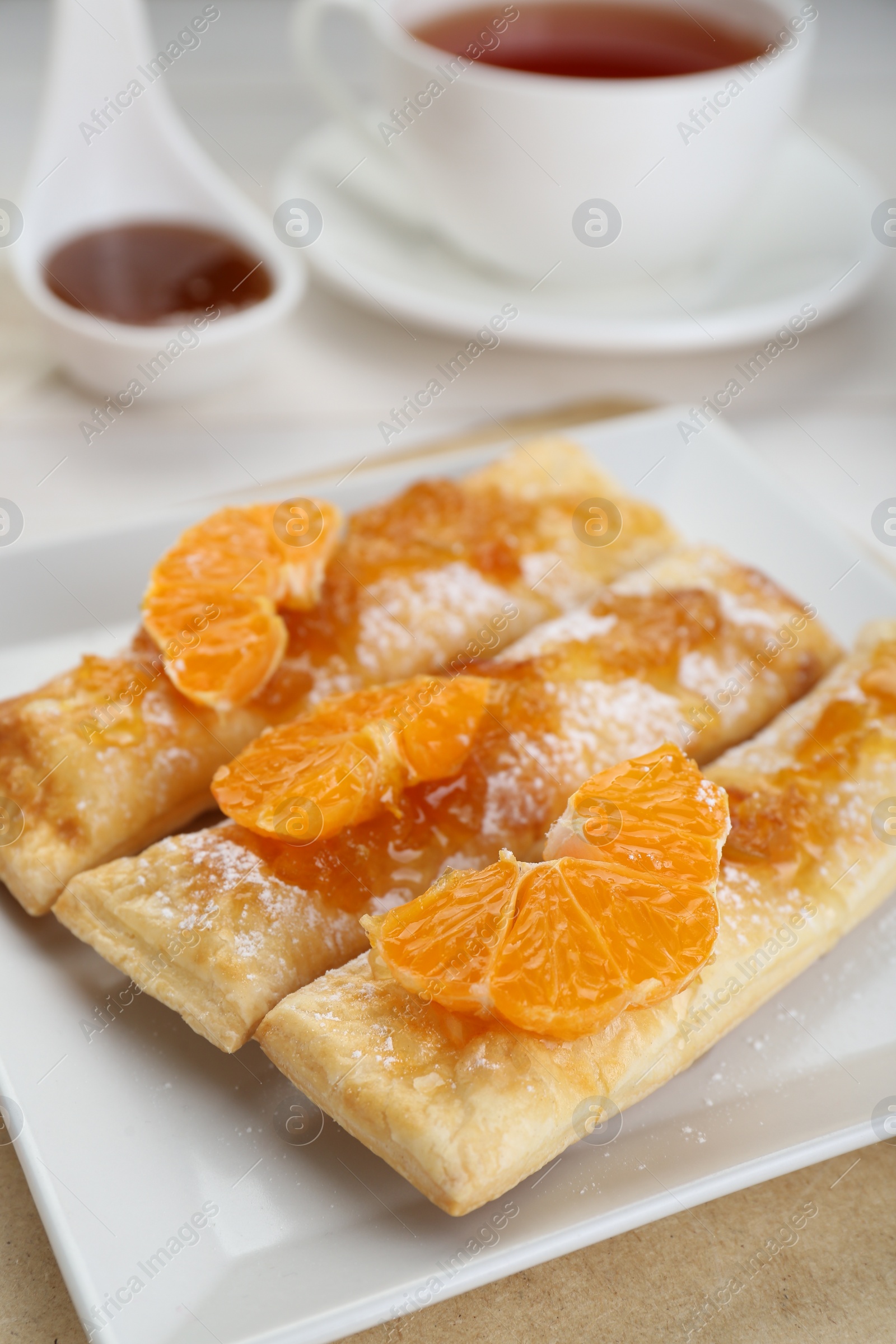 Photo of Fresh tasty puff pastry with sugar powder and tangerines on table, closeup