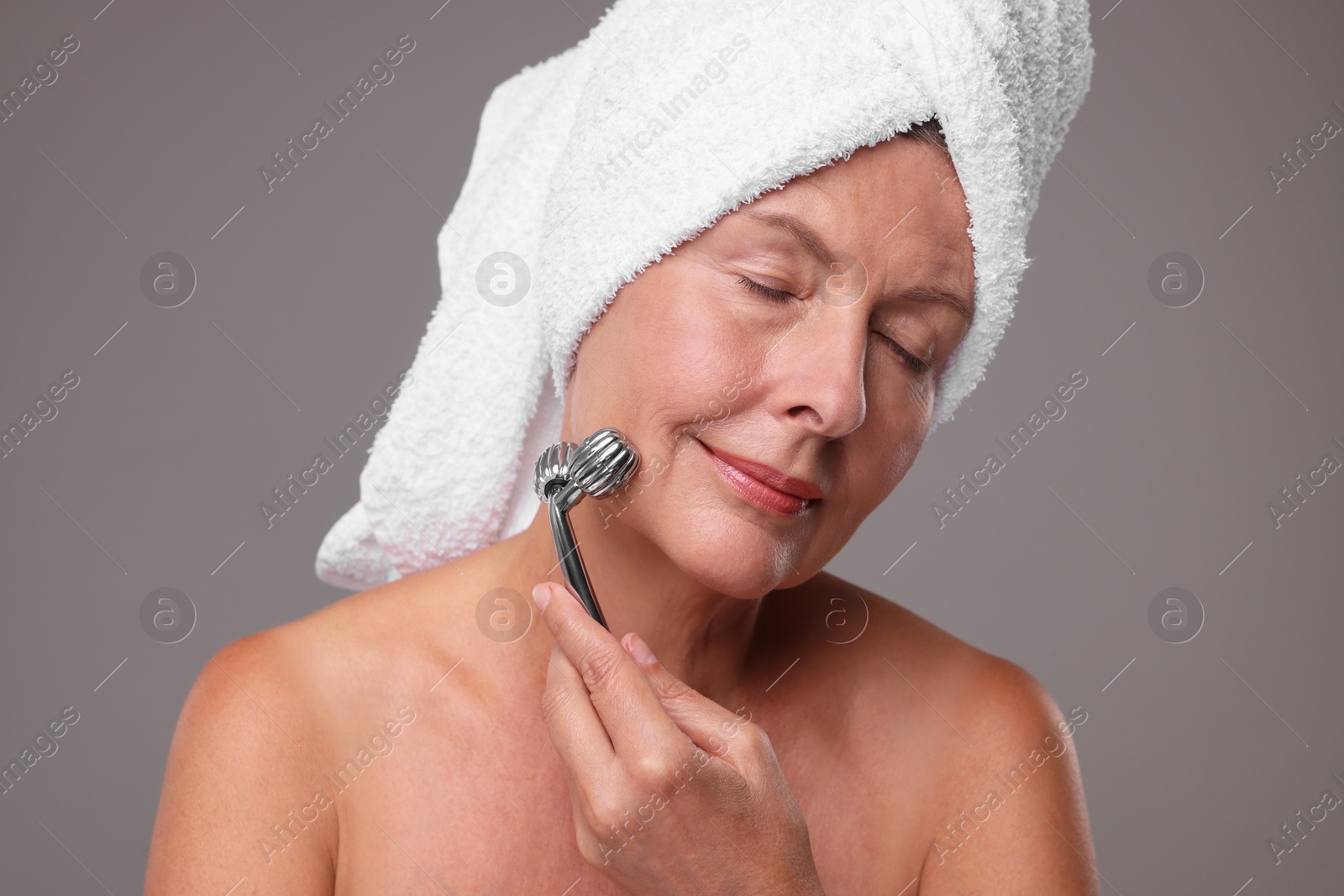 Photo of Woman massaging her face with metal roller on grey background