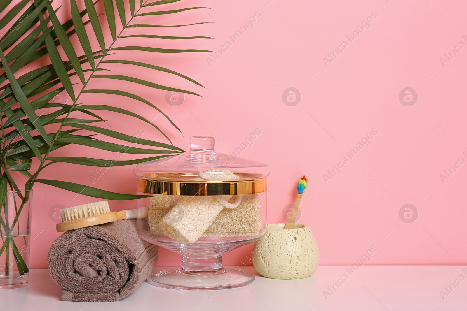 Photo of Composition of glass jar with luffa sponges on table near pink wall. Space for text