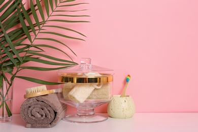 Photo of Composition of glass jar with luffa sponges on table near pink wall. Space for text