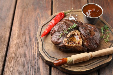 Delicious roasted beef meat served with sauce and spices on wooden table. Space for text