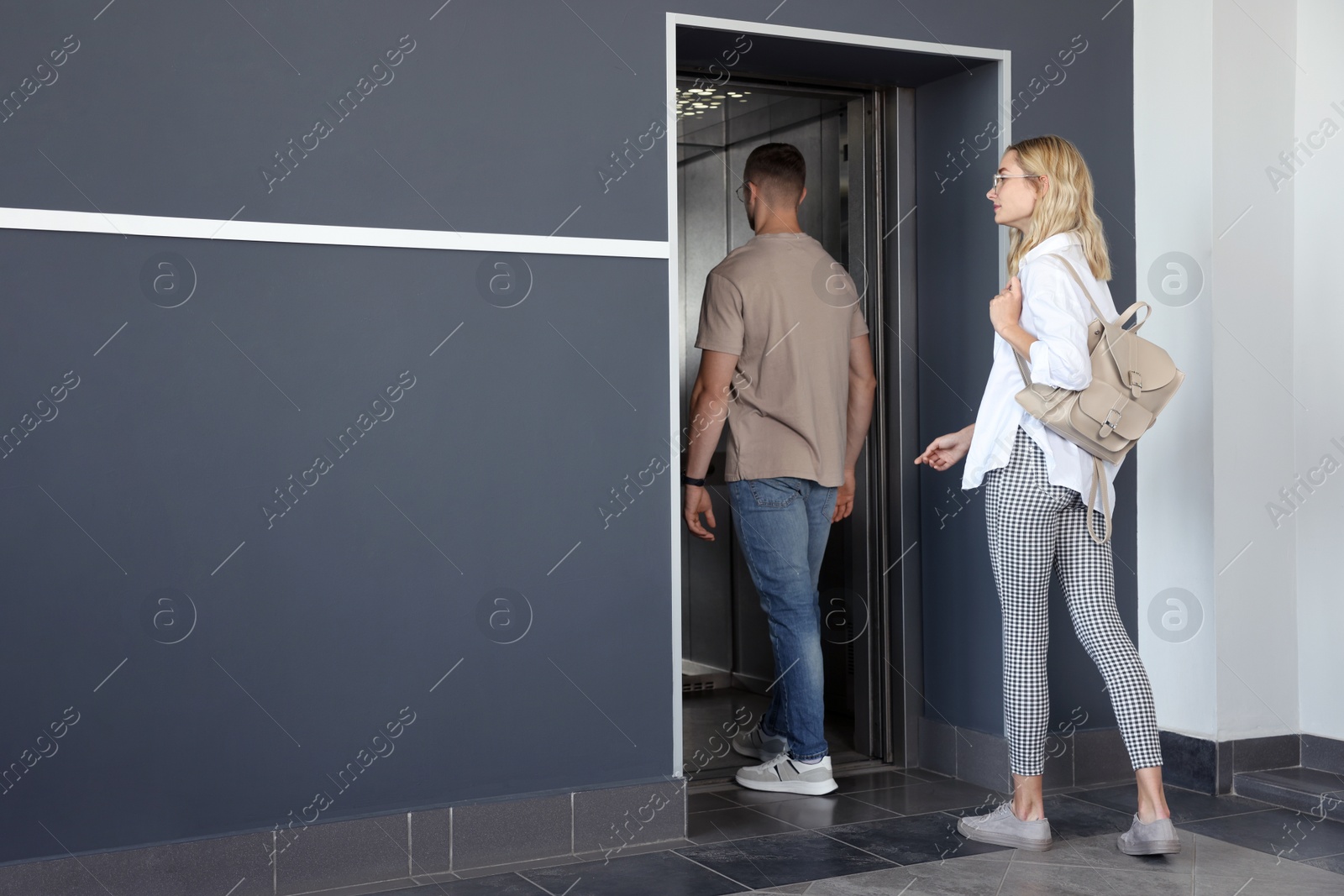 Photo of Young couple entering modern elevator, back view