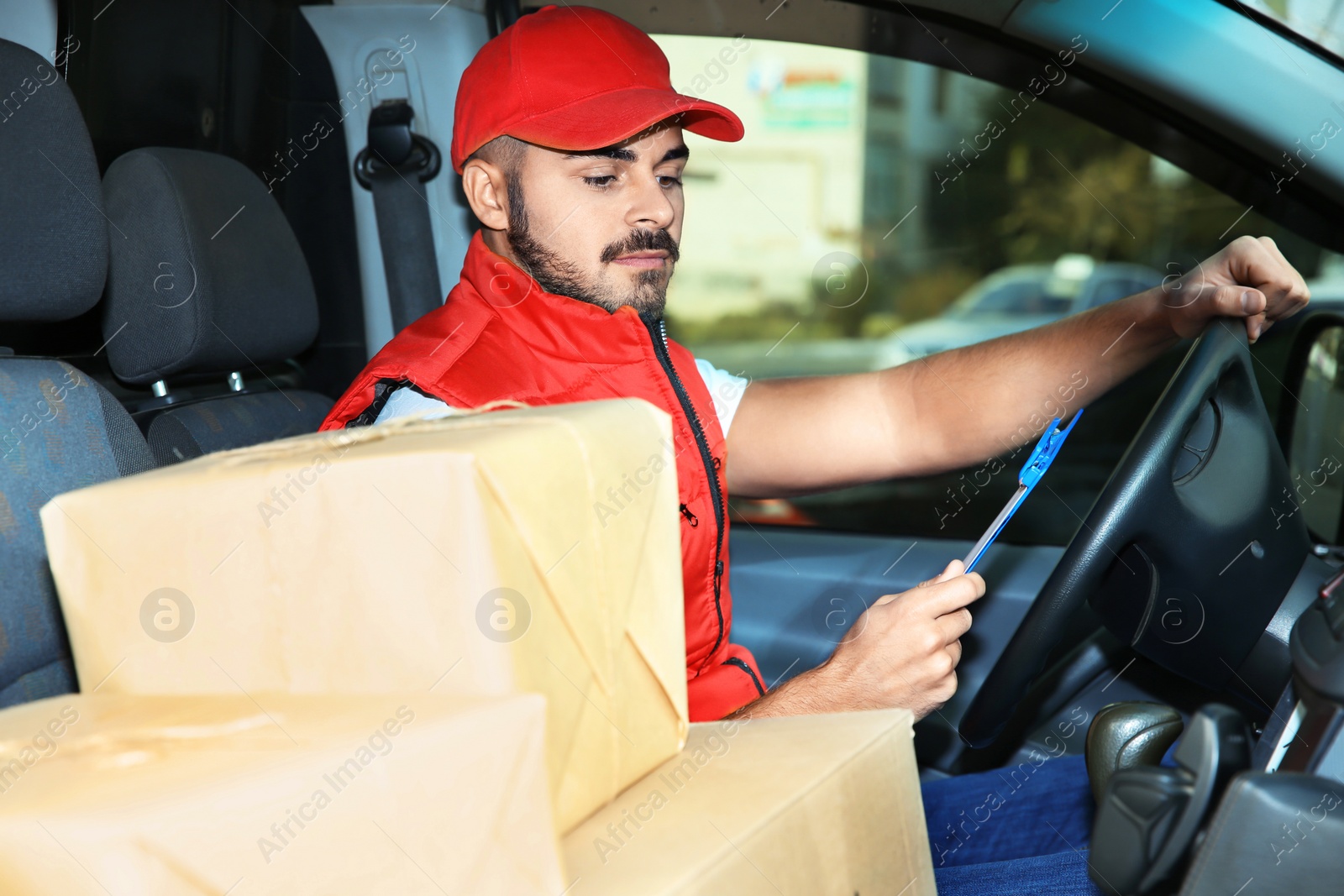 Photo of Young courier checking amount of parcels in delivery van