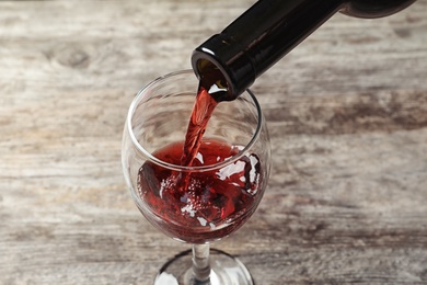 Pouring delicious red wine into glass on wooden background