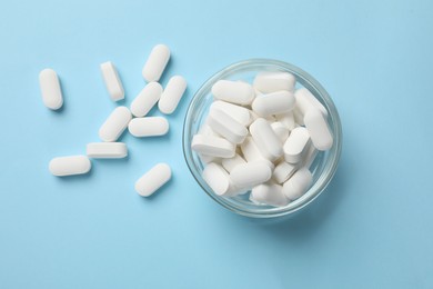 Photo of Vitamin capsules in bowl on light blue background, top view