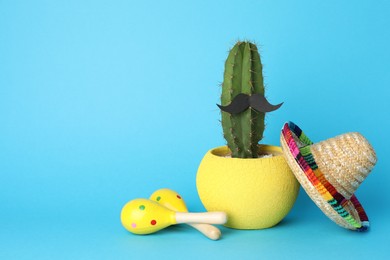 Photo of Mexican sombrero hat, cactus with fake mustache and maracas on light blue background, space for text