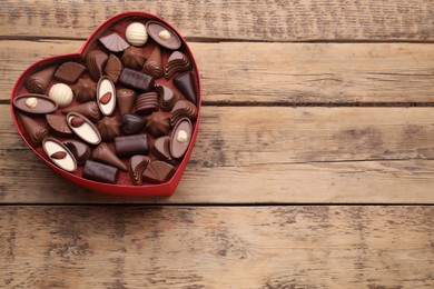 Photo of Heart shaped box with delicious chocolate candies on wooden table, top view. Space for text