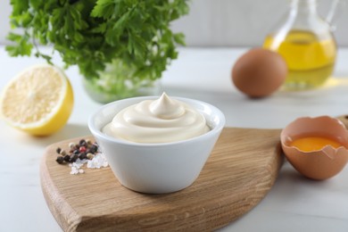 Tasty mayonnaise sauce in bowl, spices and ingredients on white table, closeup