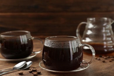 Photo of Hot coffee in glass cups, spoons and beans on wooden table, closeup