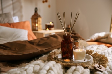 Photo of Air reed freshener and burning candles on bed indoors, space for text. Interior elements