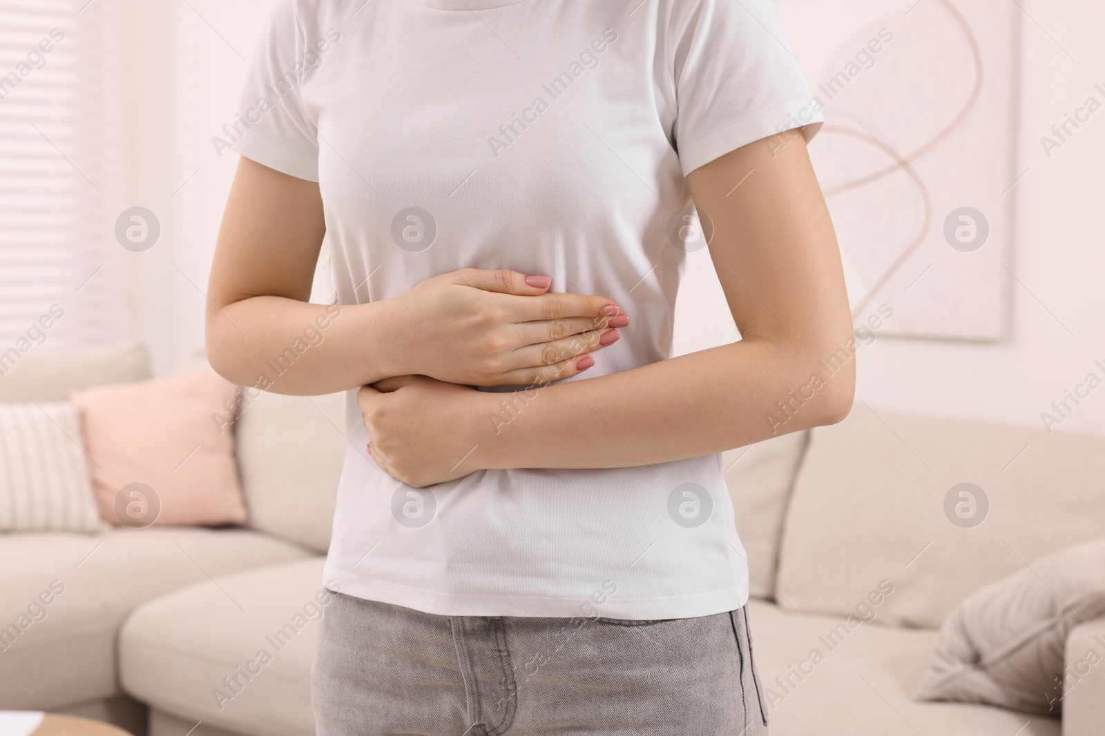 Photo of Young woman suffering from stomach pain at home, closeup