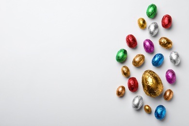 Photo of Chocolate eggs wrapped in colorful foil on white background, flat lay. Space for text