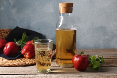 Photo of Delicious cider and red apples with green leaves on wooden table