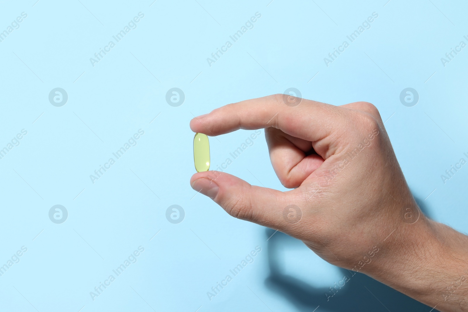 Photo of Man holding pill on light blue background, closeup
