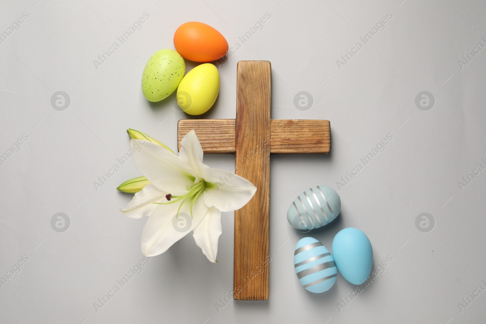 Photo of Wooden cross, painted Easter eggs and lily flowers on grey background, flat lay