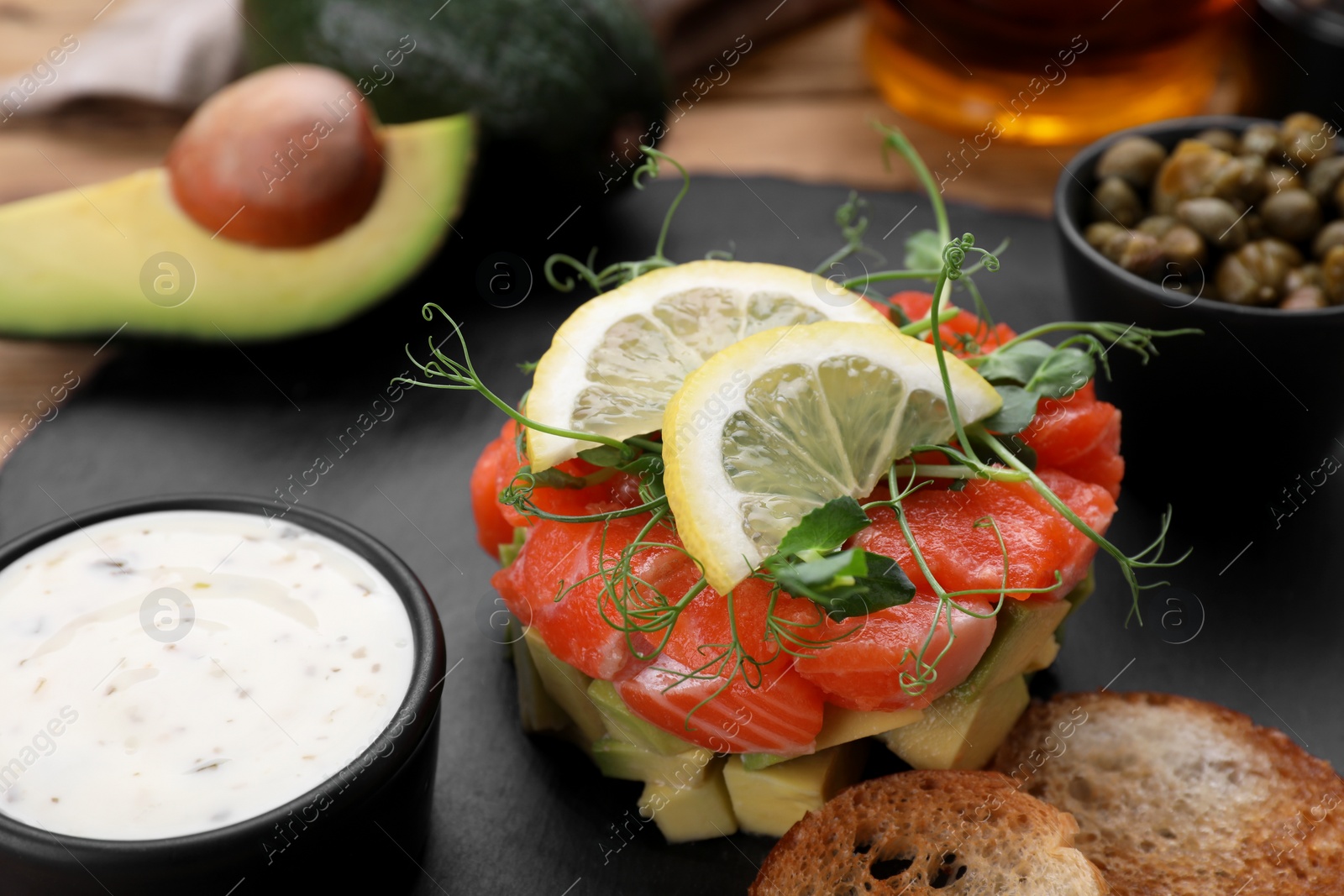 Photo of Delicious salmon tartare served with avocado, sauce and croutons on table, closeup