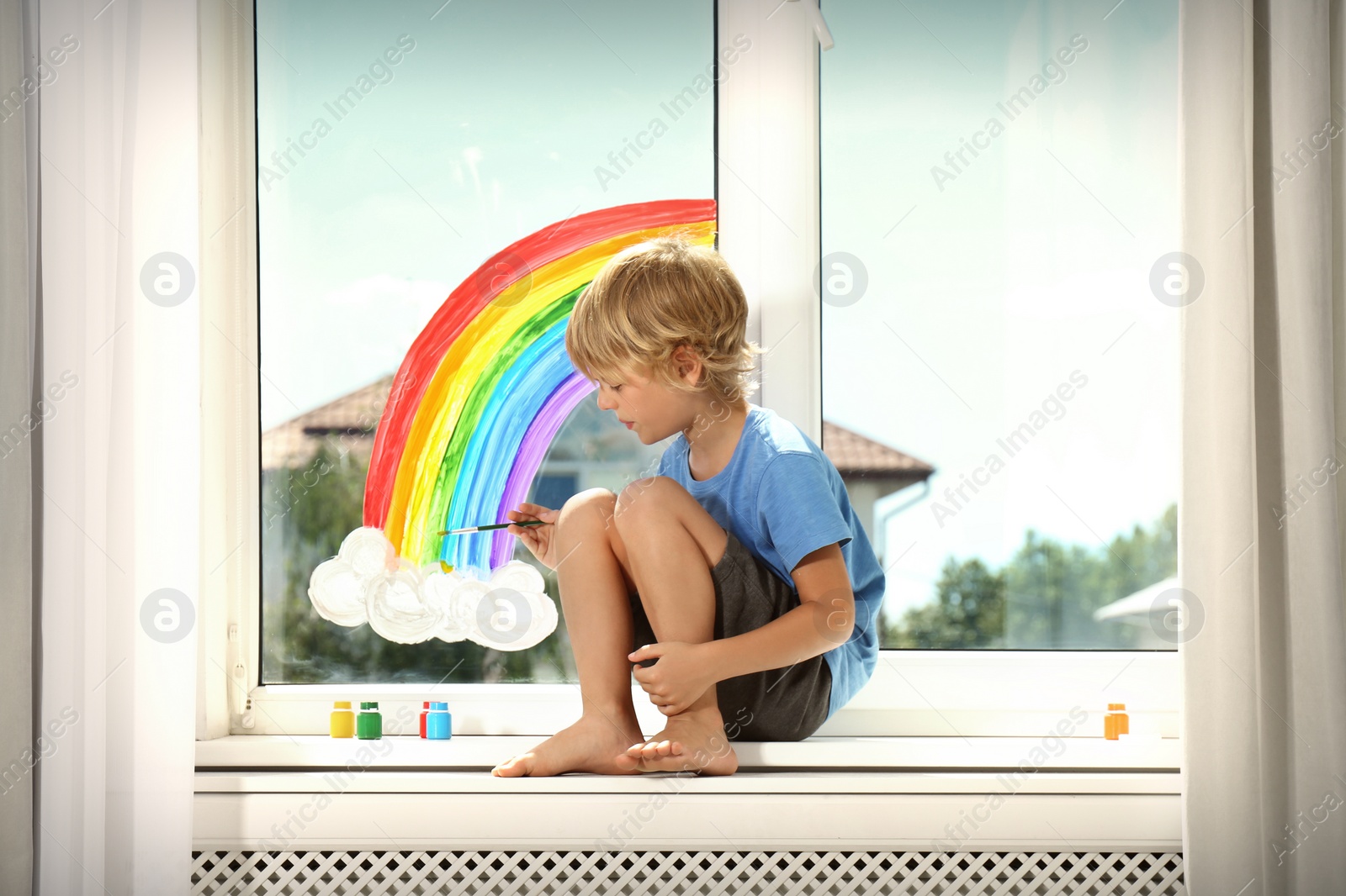 Photo of Little boy drawing rainbow on window indoors. Stay at home concept