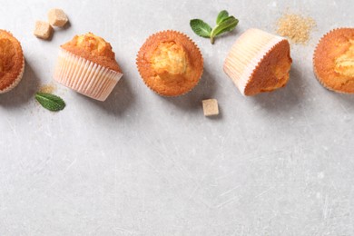 Photo of Delicious sweet muffins and brown sugar on light grey textured table, flat lay. Space for text
