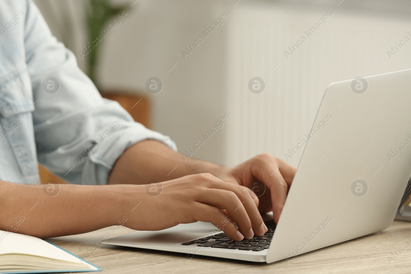 Photo of African American man typing on laptop at wooden table indoors, closeup