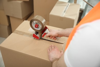 Photo of Worker taping cardboard box indoors, closeup view