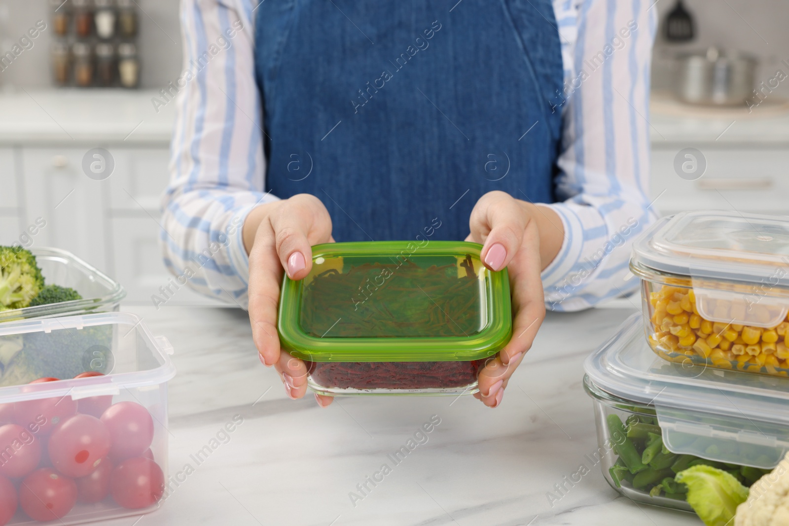 Photo of Woman holding glass container with cut fresh red beets at white marble table in kitchen, closeup. Food storage