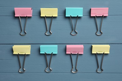 Photo of Colorful binder clips on blue wooden table, flat lay