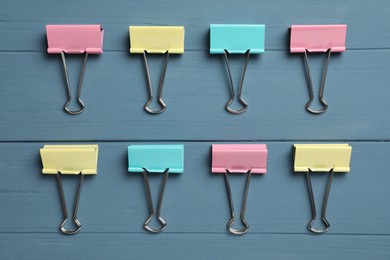 Colorful binder clips on blue wooden table, flat lay