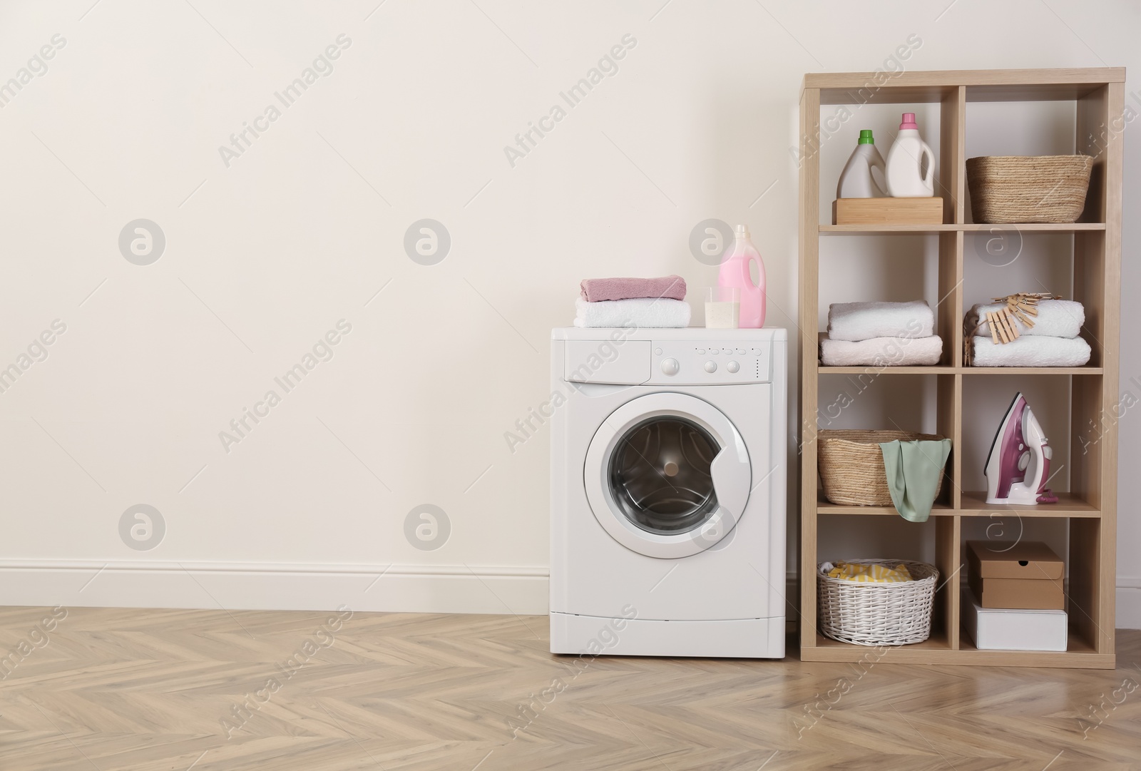 Photo of Laundry room interior with modern washing machine and shelving unit near white wall. Space for text