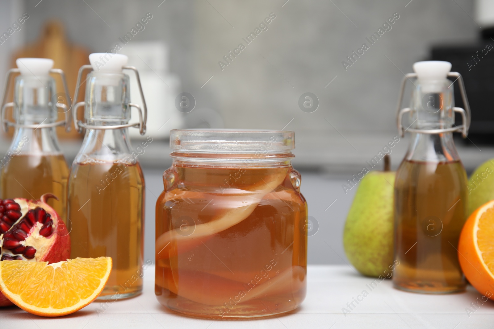 Photo of Homemade fermented kombucha and fresh fruits on white table in kitchen