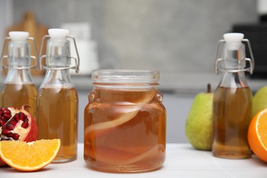 Photo of Homemade fermented kombucha and fresh fruits on white table in kitchen