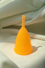 Photo of Menstrual cup on light fabric. Reusable female hygiene product