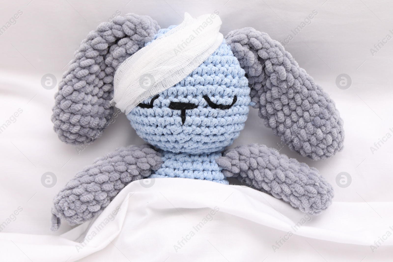 Photo of Toy cute bunny with bandage under blanket in bed