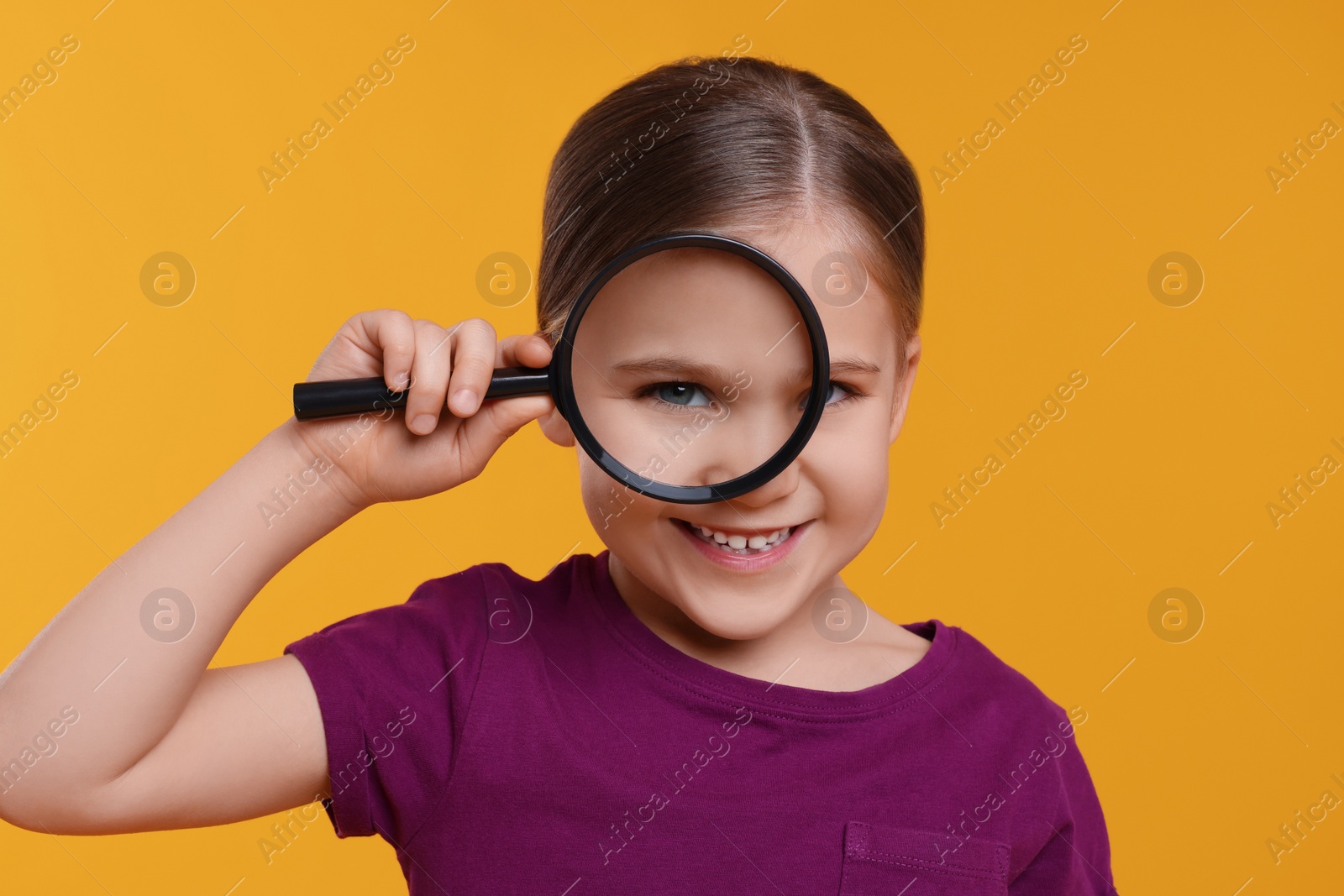 Photo of Cute little girl looking through magnifier on orange background