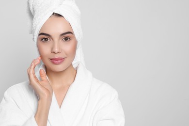 Young woman in bathrobe with towel on light grey background, space for text. Spa treatment