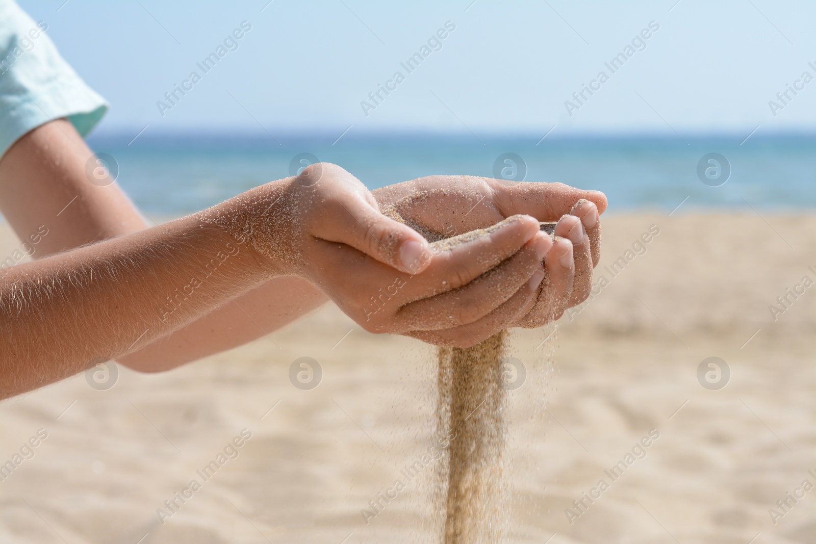 Photo of Child pouring sand from hands on beach near sea, closeup. Fleeting time concept