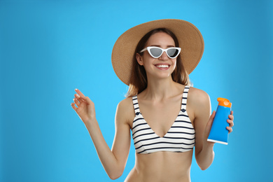 Young woman with sun protection cream on light blue background