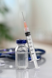 Glass vial, syringe and stethoscope on white table, closeup