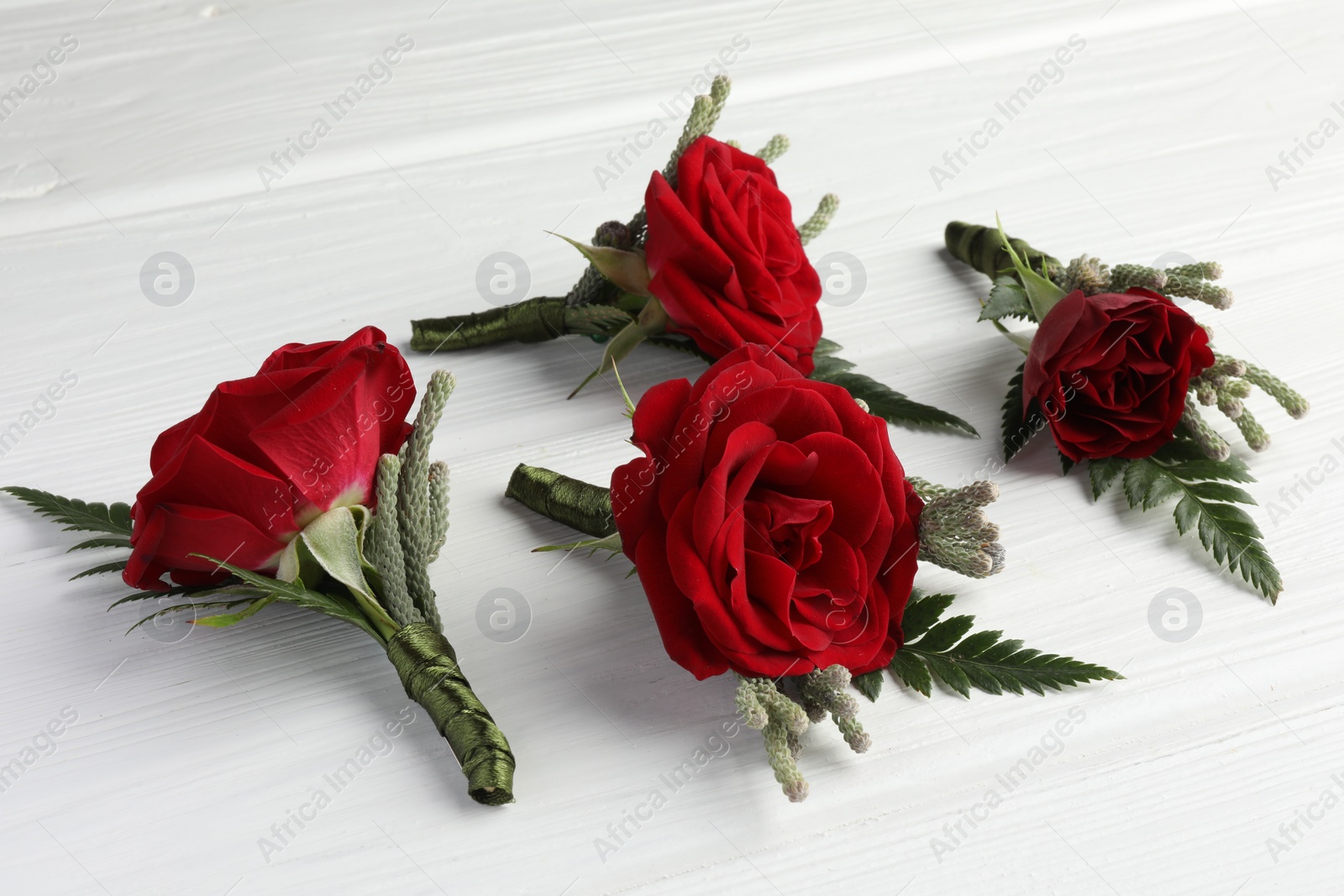 Photo of Many stylish red boutonnieres on white wooden table