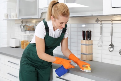 Photo of Female janitor cleaning kitchen counter with brush in house