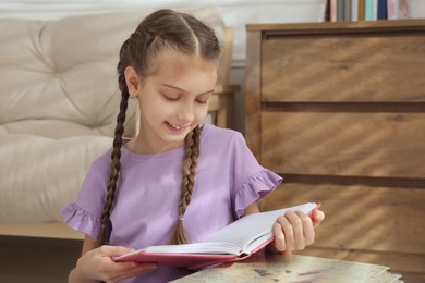 Photo of Cute little girl reading book at home