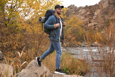 Man with backpack crossing mountain river on autumn day