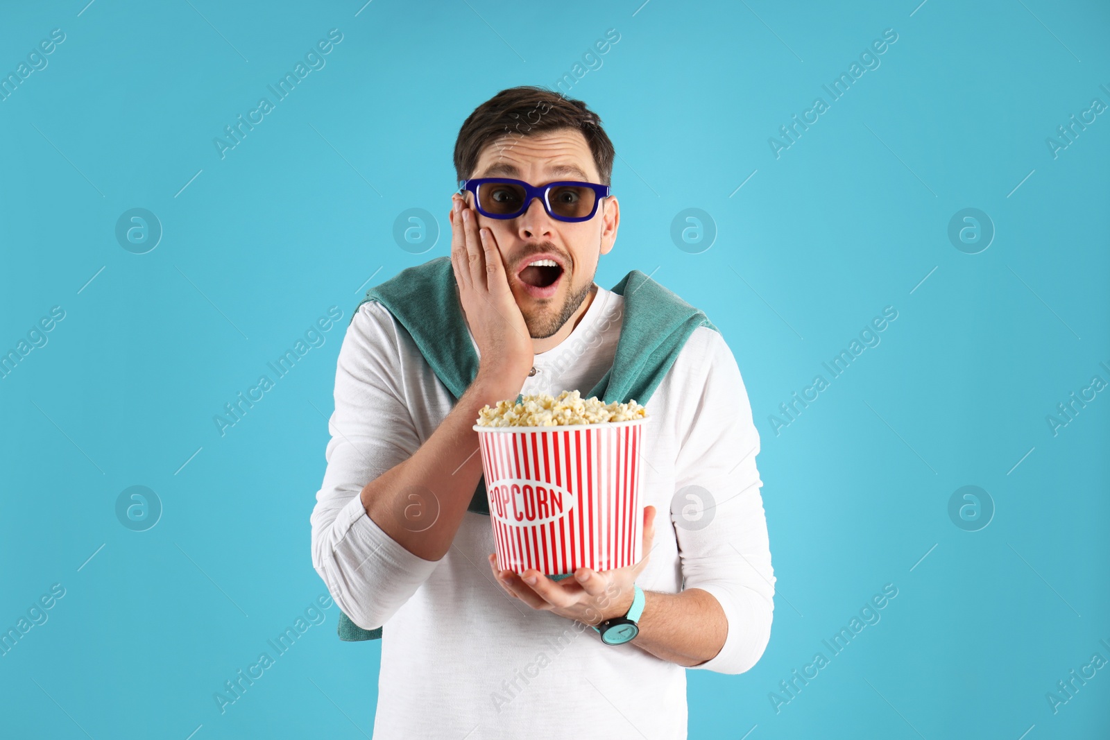 Photo of Emotional man with 3D glasses and tasty popcorn on color background