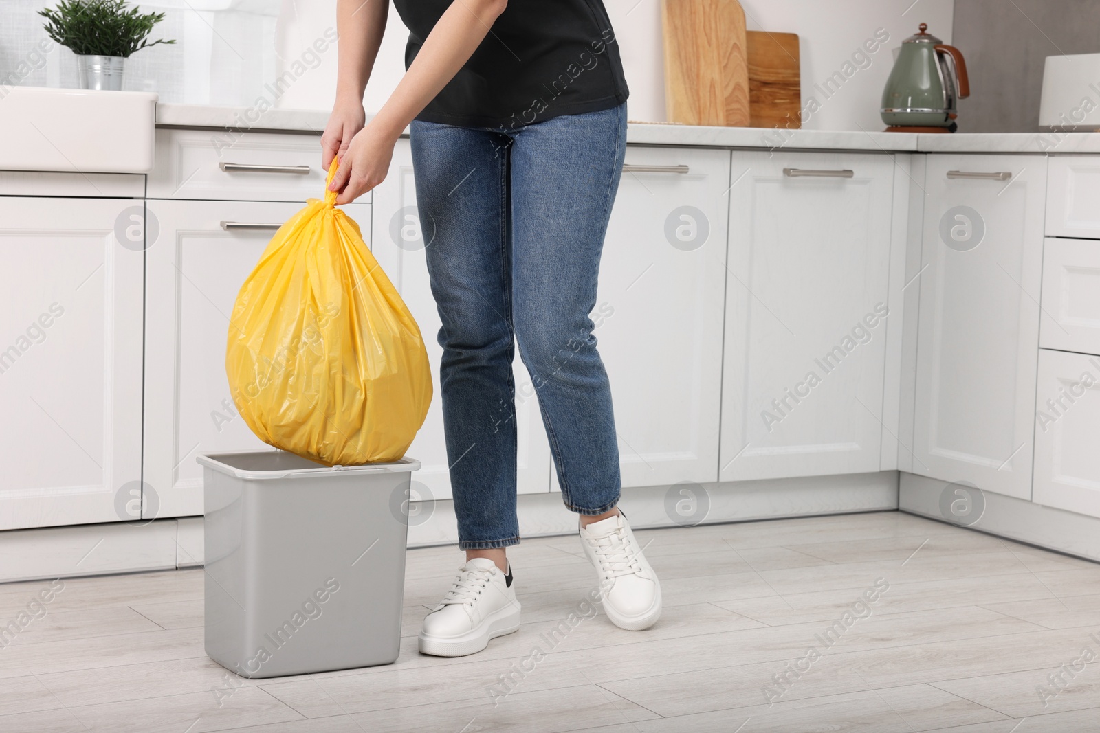 Photo of Woman taking garbage bag out of trash bin in kitchen, closeup