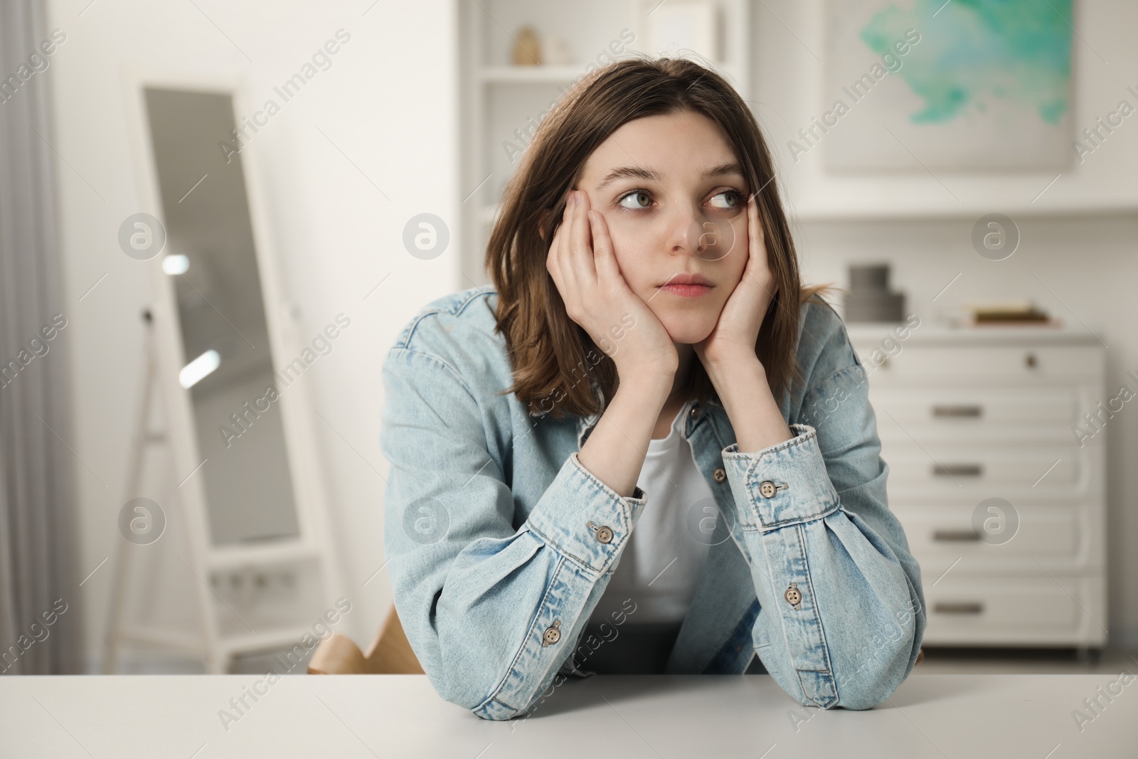 Photo of Sad young woman sitting at white table in room