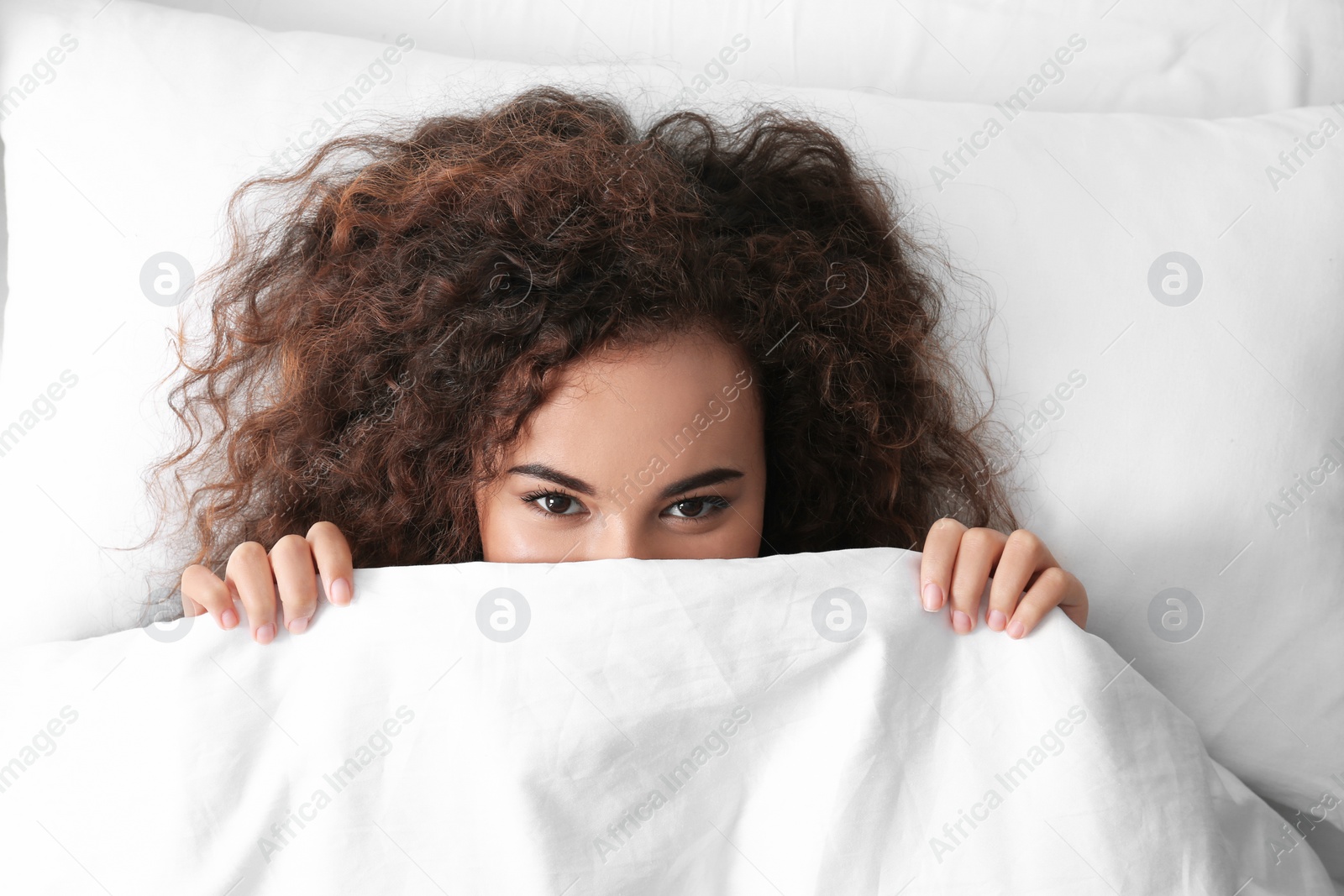 Photo of Young African-American woman lying under blanket, top view. Bedtime