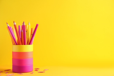 Pencils with felt pens in holder and paper clips on yellow background. Space for text