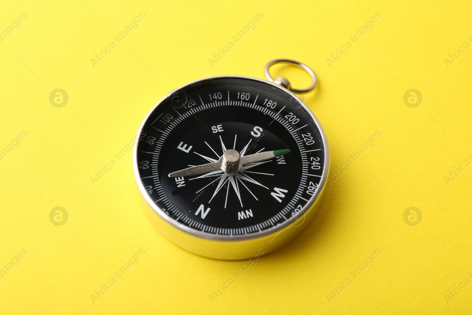 Photo of One compass on yellow background, closeup. Tourist equipment