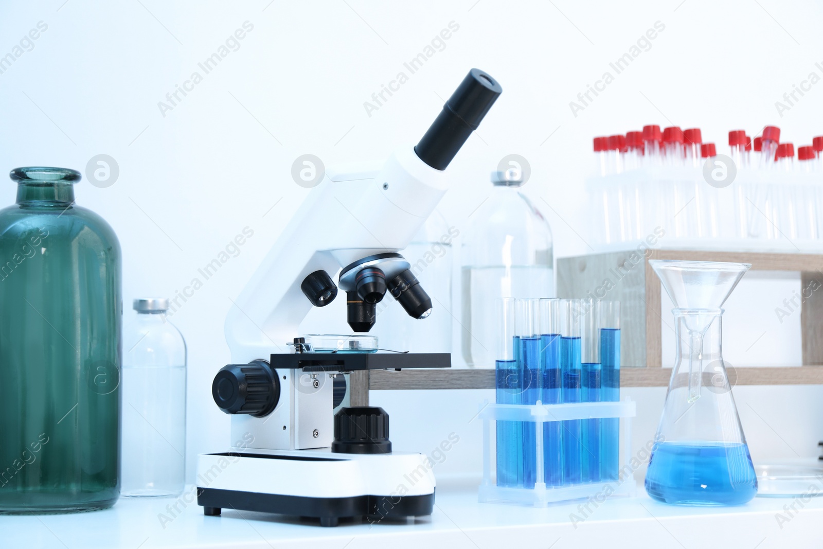 Photo of Laboratory analysis. Different glassware with blue liquid and microscope on white table indoors