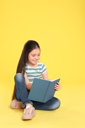 Cute little girl reading book on color background, space for text