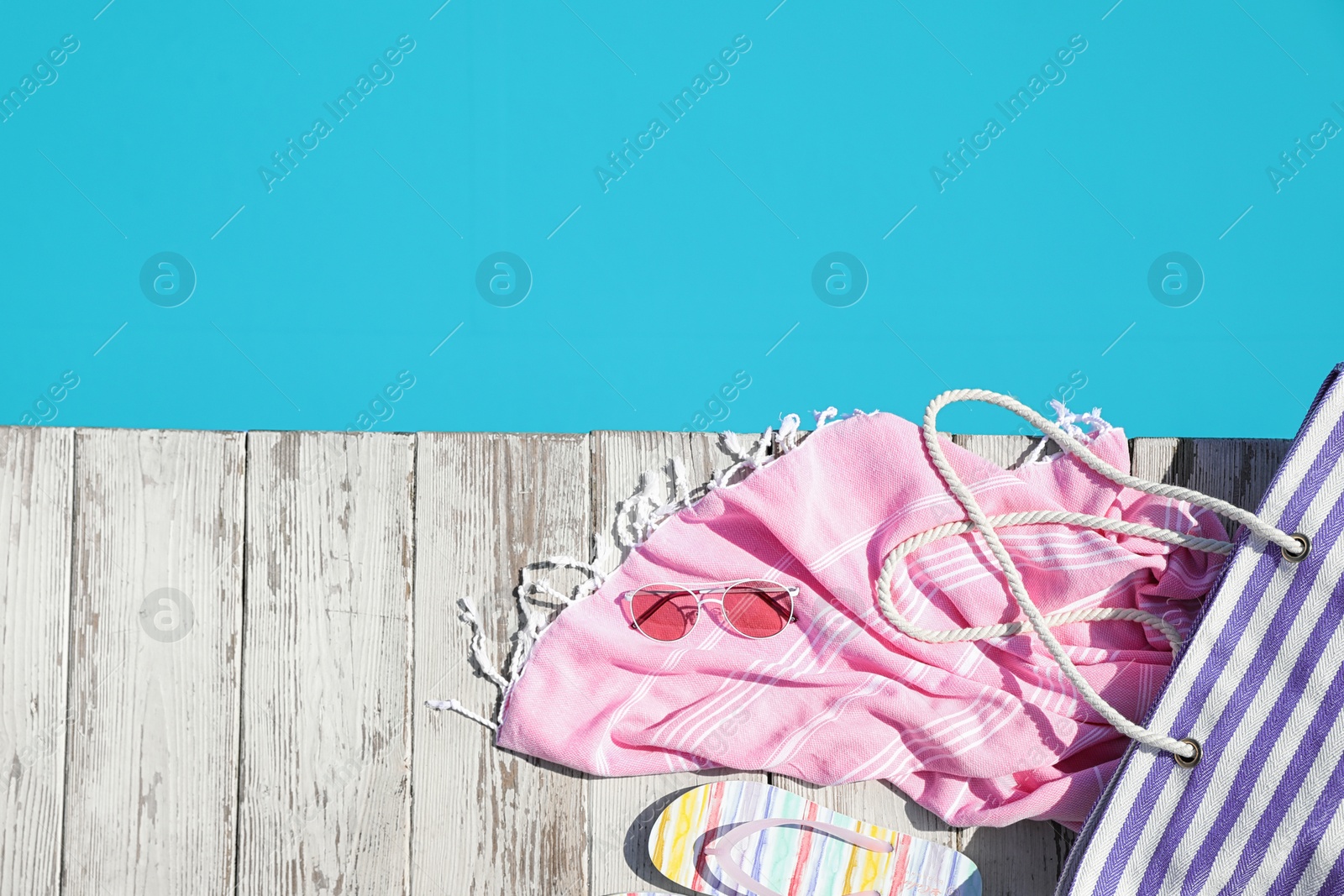 Photo of Beach accessories on wooden deck near outdoor swimming pool, flat lay. Space for text